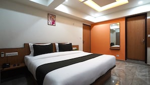 A hotel room with a large bed, a ceiling fan, a wall-mounted TV, and a wooden door. - hotel orange tree (Ahmedabad)