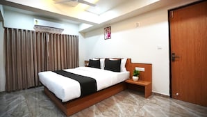 A hotel room with a bed, bedside table, nightstand, and a door. - hotel orange tree (Ahmedabad)