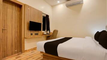 A hotel room with a bed, a desk with a chair, a flat-screen TV, and an air conditioning unit.