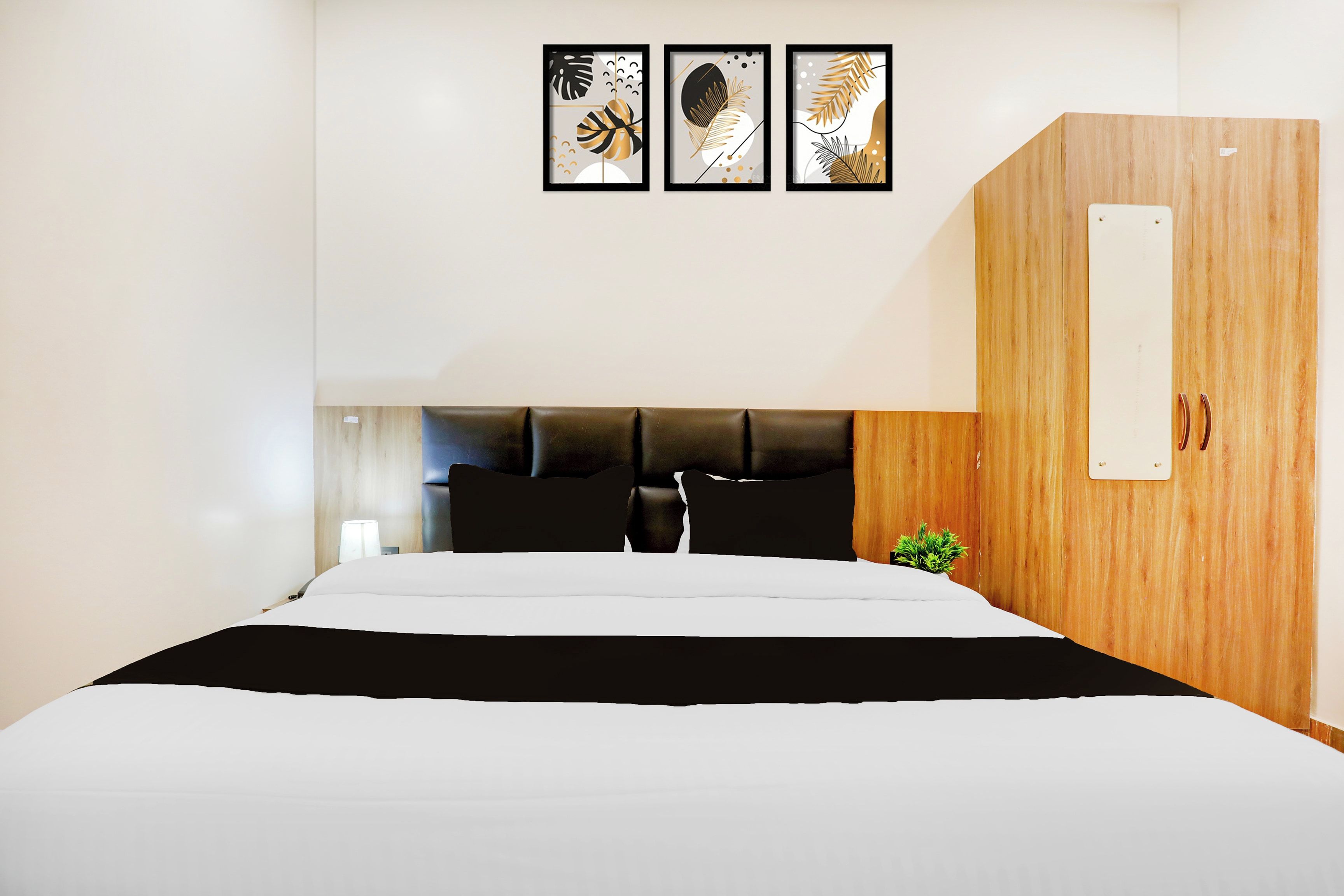 Quarto de hotel com cama, guarda-roupa de madeira e três obras de arte emolduradas na parede.
