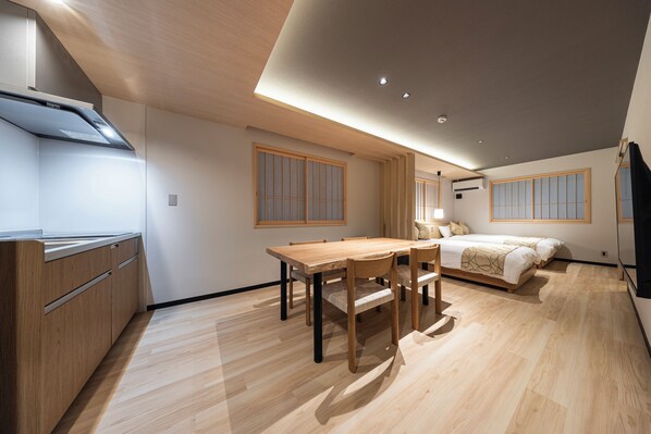 Una habitación de hotel moderna con una mesa de comedor de madera, una cama con cabecera y una kitchenette.