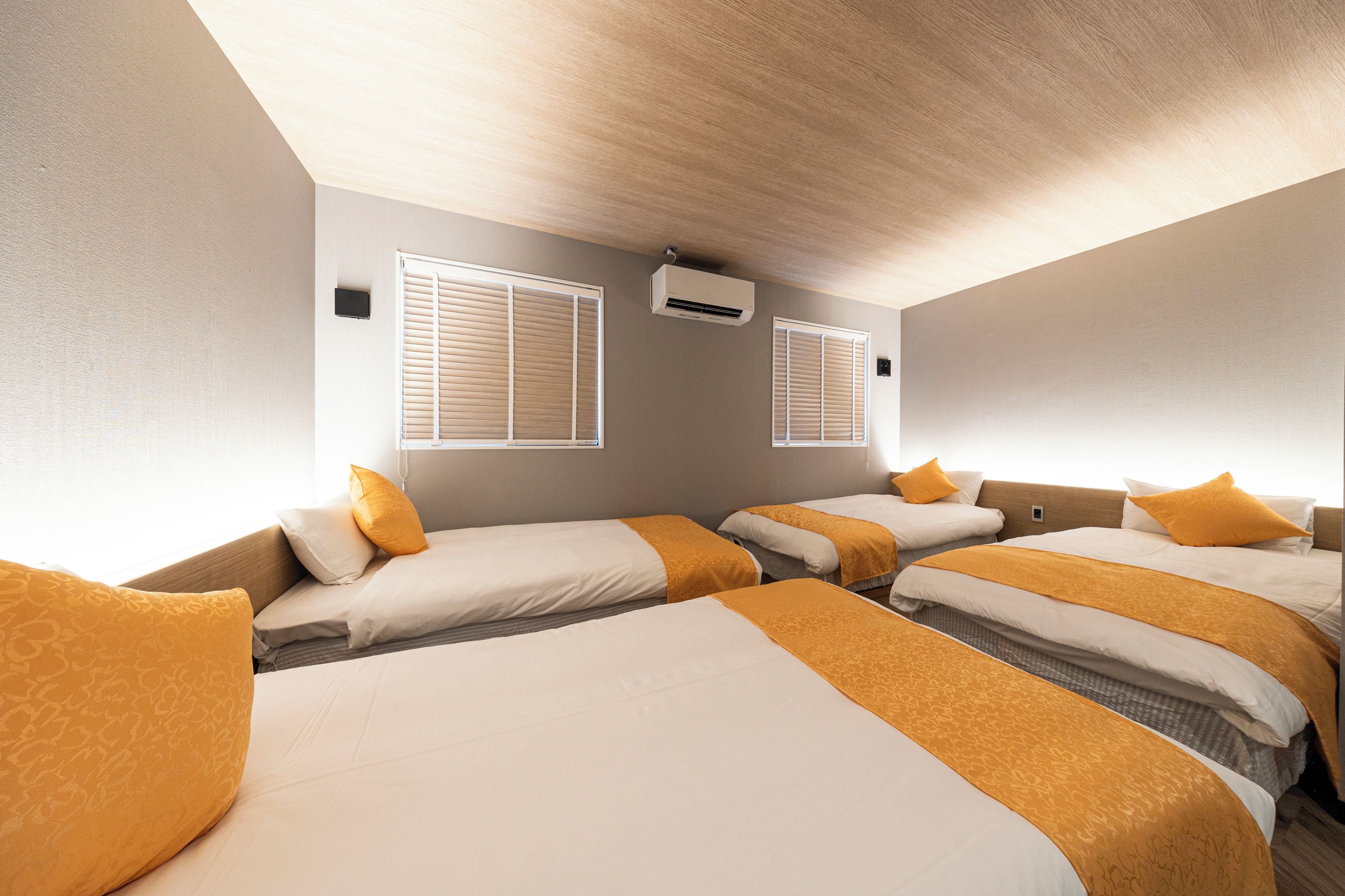 A hotel room with four beds arranged in a row, each with white bedding and orange accents.