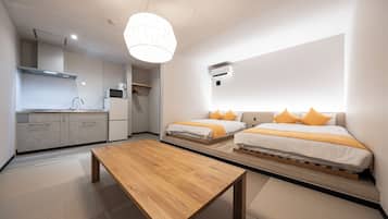 Habitación de hotel moderna con área de cocina, una mesa de madera y dos camas con almohadas naranjas.