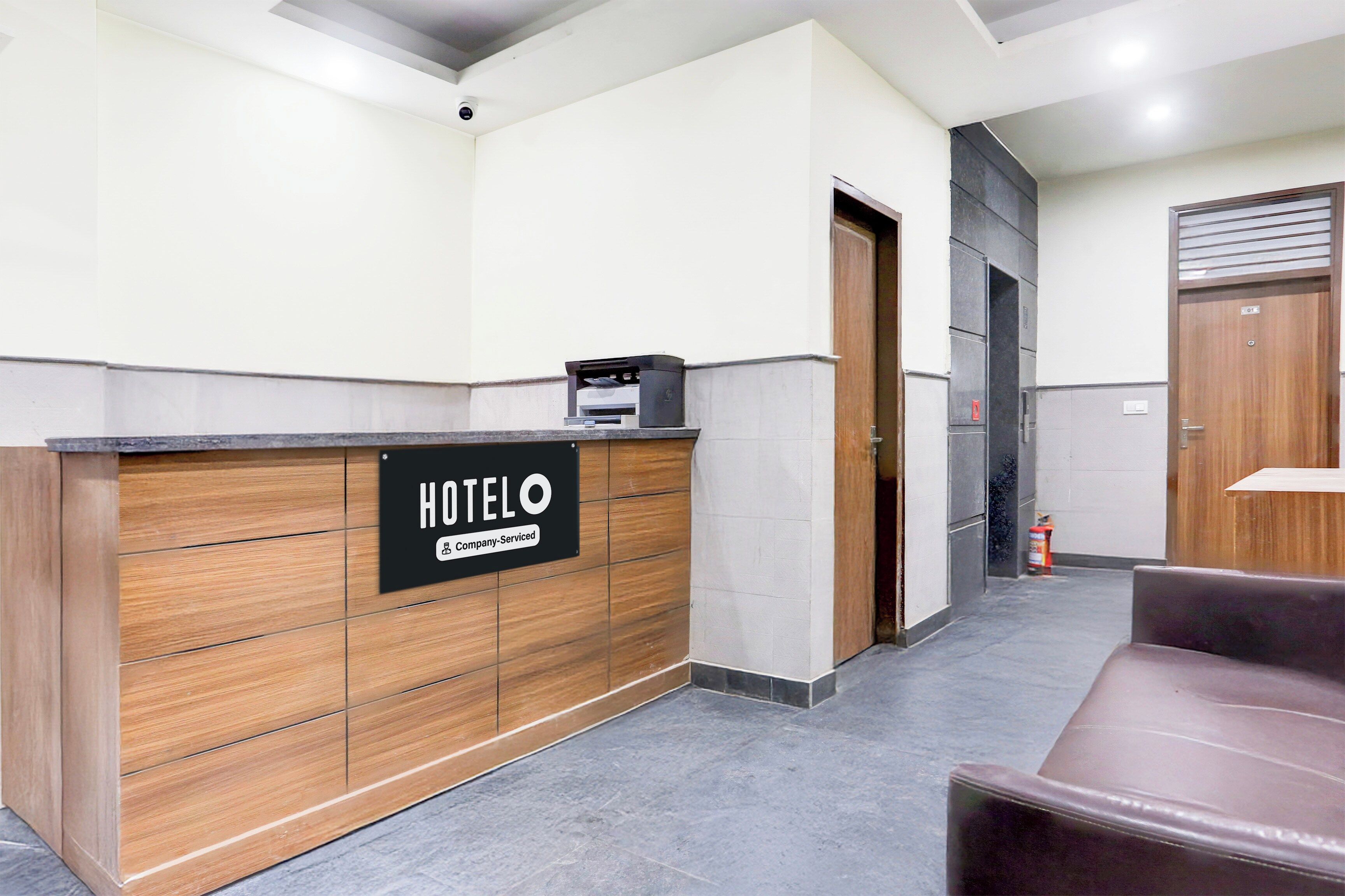 A hotel reception area with a wooden reception desk, a sign indicating it's company-serviced, and a fire extinguisher.