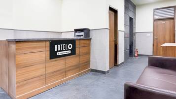 A hotel reception area with a wooden reception desk, a sign indicating it's company-serviced, and a fire extinguisher.