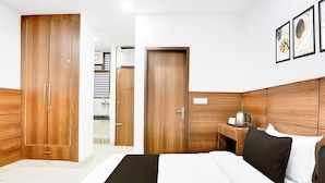 Una camera d'albergo con un letto grande, un armadio in legno, un comodino con un bollitore e un quadro appeso al muro.