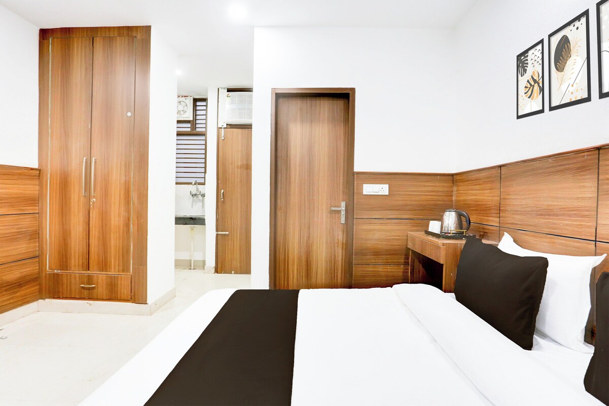 Habitación de hotel con una cama grande, armario de madera, mesita de noche con hervidor y un cuadro enmarcado en la pared.