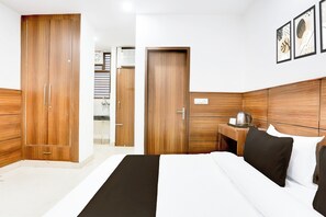 Habitación de hotel con una cama grande, armario de madera, mesita de noche con hervidor y un cuadro enmarcado en la pared.
