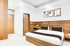 Una habitación de hotel con una cama grande, cabecero de madera, mesitas de noche, un armario y tres cuadros enmarcados en la pared.