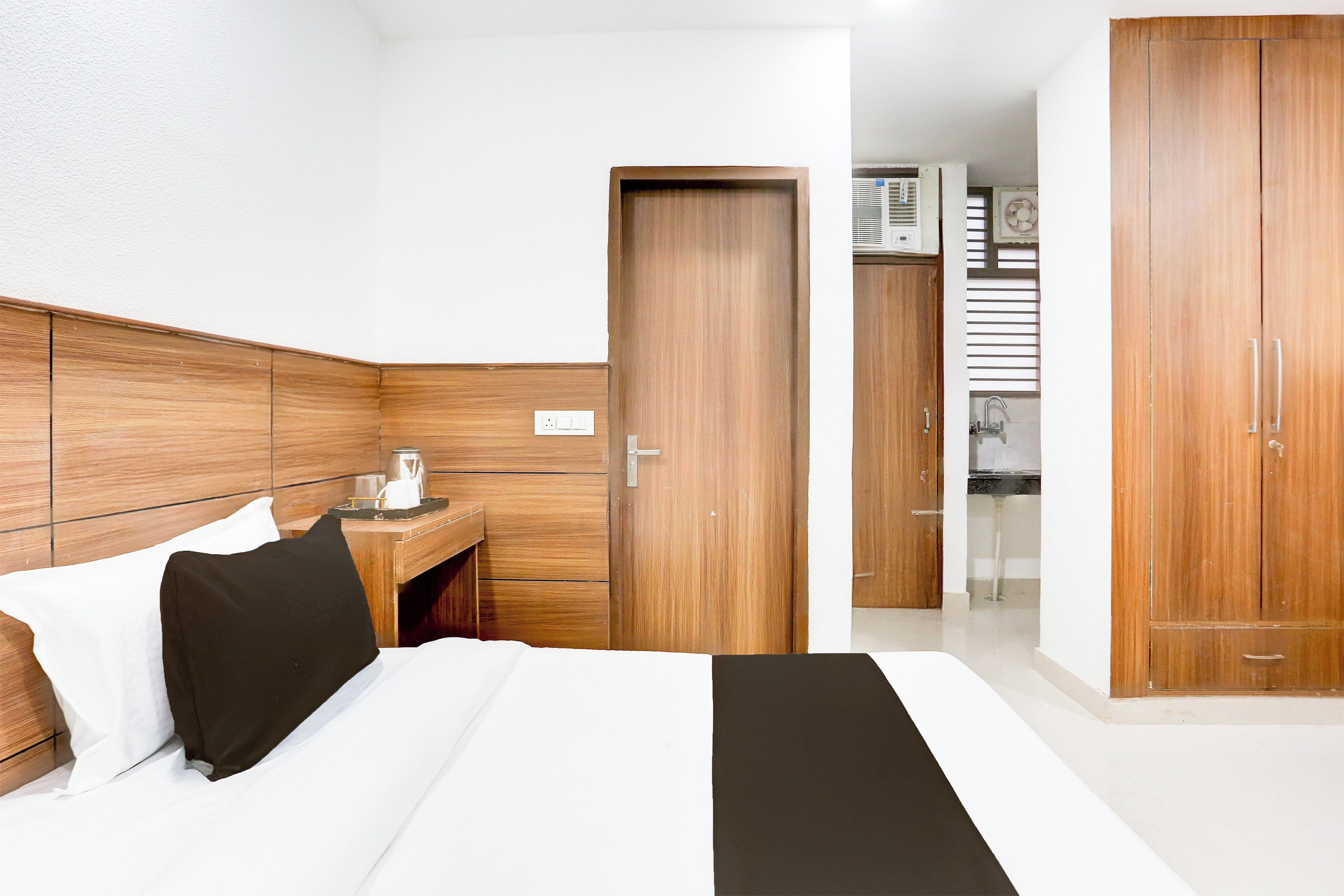 A hotel room with a bed, a bedside table, a wardrobe, and a kitchenette area.