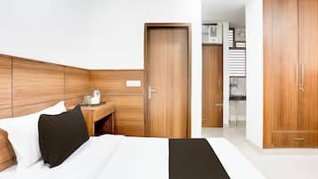 A hotel room with a bed, a bedside table, a wardrobe, and a kitchenette area.