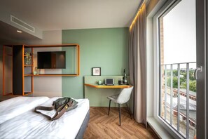 Ein Hotelzimmer mit einem Bett, einem Schreibtisch mit Stuhl, einem Fernseher und einem Fenster mit Blick.