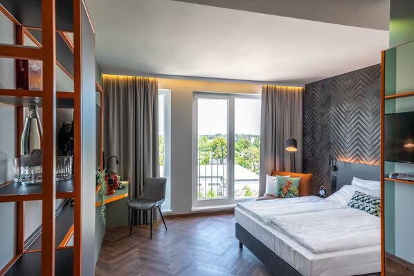 Ein modernes Hotelzimmer mit einem großen Bett, einem Schreibtisch mit Stuhl, einem Balkon mit Vorhängen und einer Wand mit Fischgrätmuster.