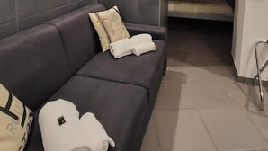 A modern room with a dark-colored sofa, a small bed, and a tiled floor. - Il Taschino Suite (Naples)