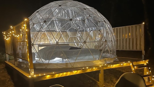 A geodesic dome structure with a table and chairs in front, surrounded by string lights.