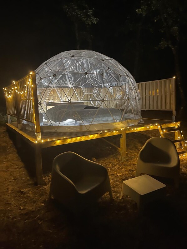 Una estructura de domo geodésico con una mesa y sillas al frente, rodeada de luces colgantes.