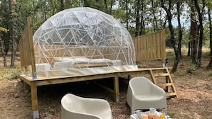 A geodesic dome structure with a bed, two chairs, and a small table with breakfast items.