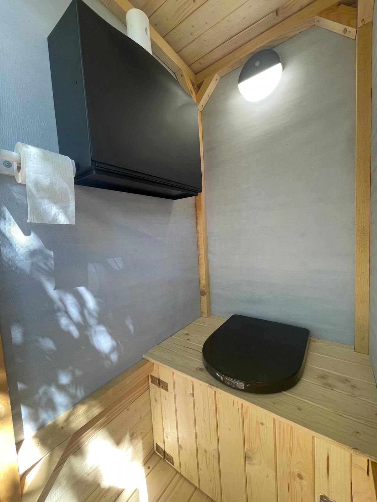 Une petite pièce en bois, avec un banc noir, un distributeur de serviettes et un luminaire au plafond.