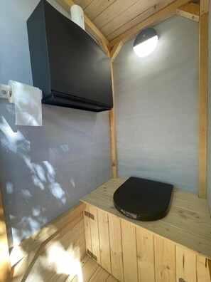 Habitació de fusta petita amb una banca negra, un dispensador de tovalloles i una làmpada al sostre.