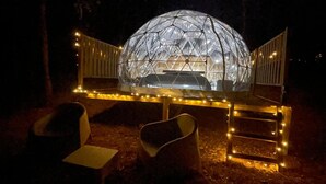 A dome-shaped structure with a seating area in front, surrounded by a fence with lights.