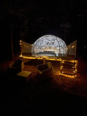 Estructura abovedada con una zona de estar al frente, rodeada por una valla con luces.