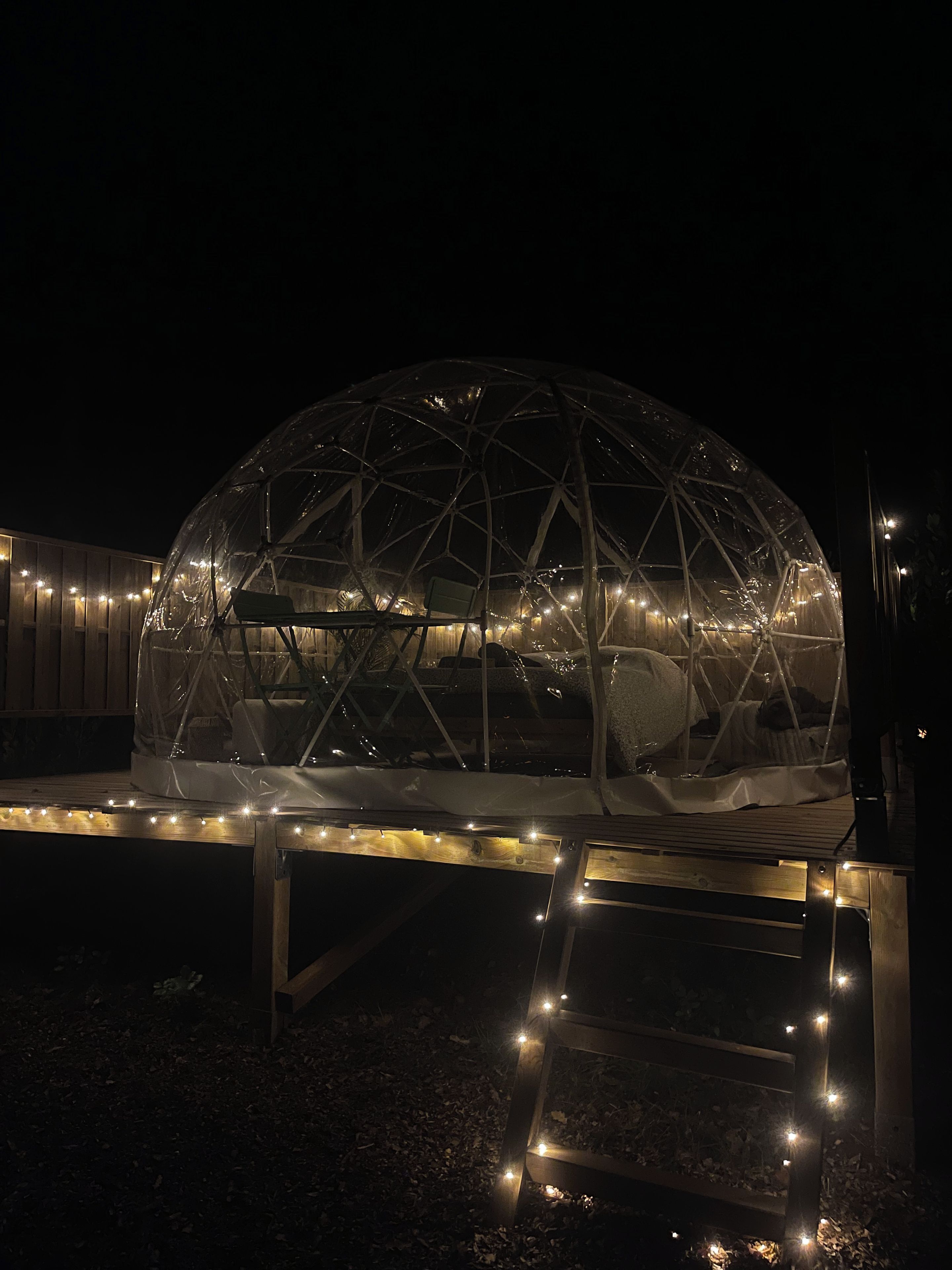 Una struttura a cupola geodetica con una panchina di fronte, circondata da luci a stringa.