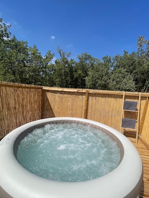 An outdoor hot tub surrounded by a wooden fence with a clear blue sky above.