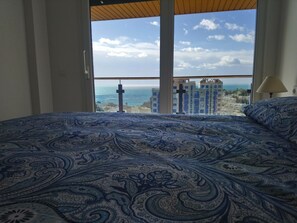 Un dormitorio con una cama grande, vista al mar y edificios al fondo.