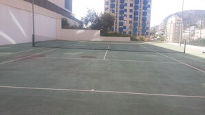 Ulkotenniskenttä, jossa on verkko, ja jonka ympärillä on rakennuksia ja taustalla vuori.