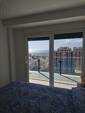 Et værelse med en stor skydedør, der fører ud til en balkon med udsigt over bygninger og vand.