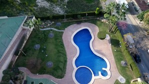 Ilmakuva uima-altaasta, jonka muoto on ainutlaatuinen. Altaan ympärillä on hyvin hoidettua nurmikkoa ja puita.