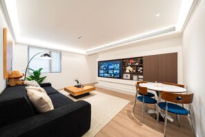 Uma sala de estar moderna com sofá, mesa de centro, mesa de jantar com cadeiras e TV fixada na parede.