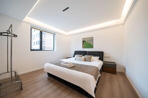 Ein modernes Schlafzimmer mit einem großen Bett, einem Fenster, einem Gemälde und einem Metallwagen.