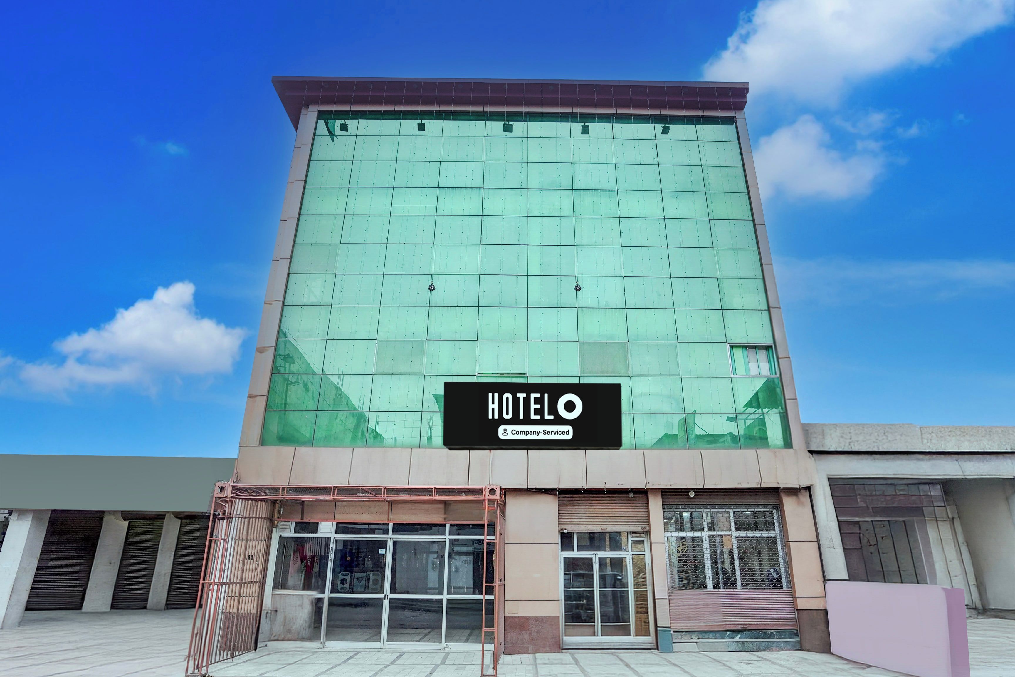 Un edificio de hotel con un amplio frente de vidrio, un letrero que indica que es un hotel de servicios corporativos y una entrada con portón.