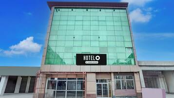 Un edificio de hotel con un amplio frente de vidrio, un letrero que indica que es un hotel de servicios corporativos y una entrada con portón.