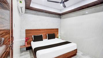 Un dormitorio moderno con cabecera de madera, cama con ropa de cama blanca, mesita de noche, un florero con flores y un ventilador de techo.