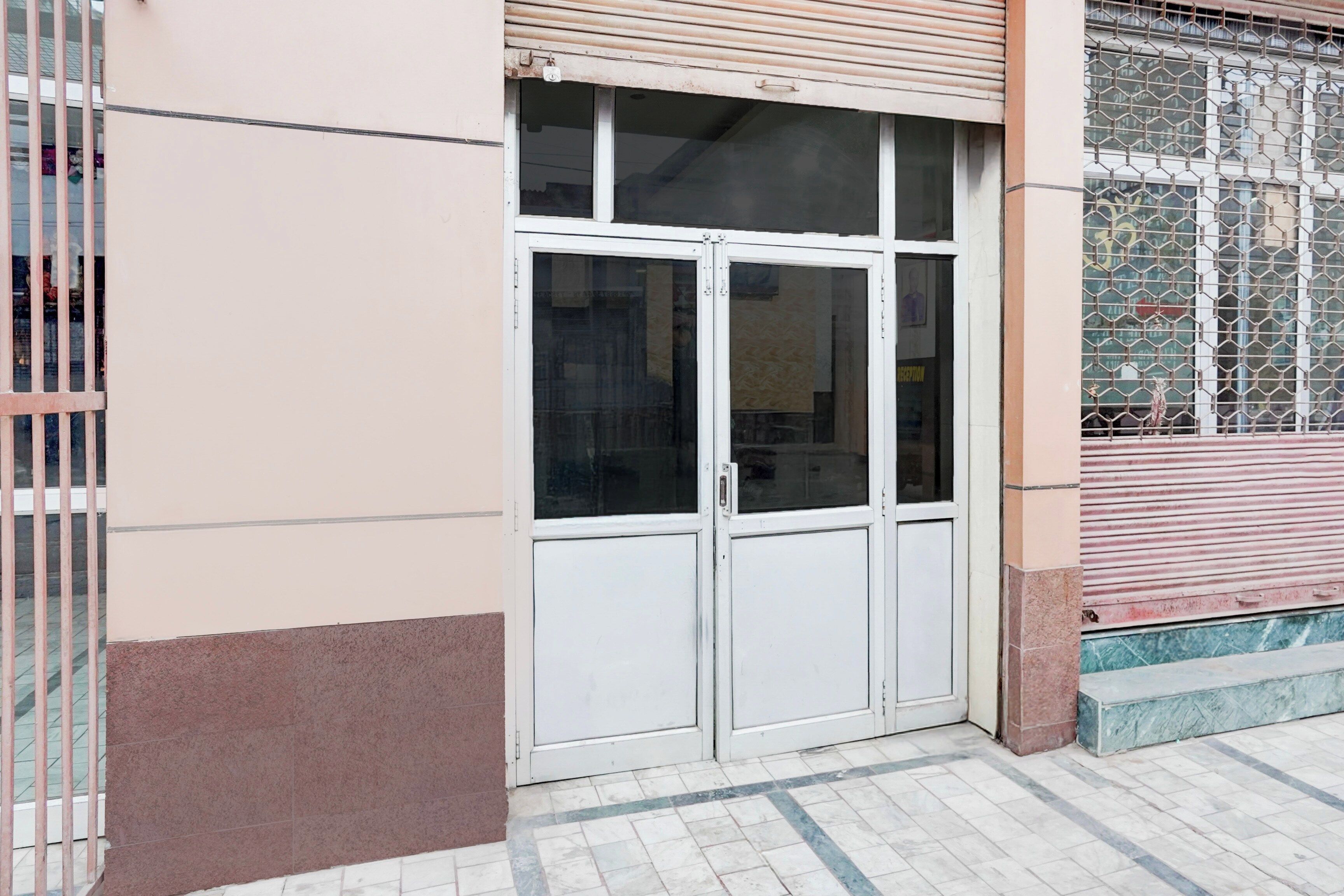 Entrada de un edificio con puertas dobles, una reja de metal y adoquinado de cerámica.
