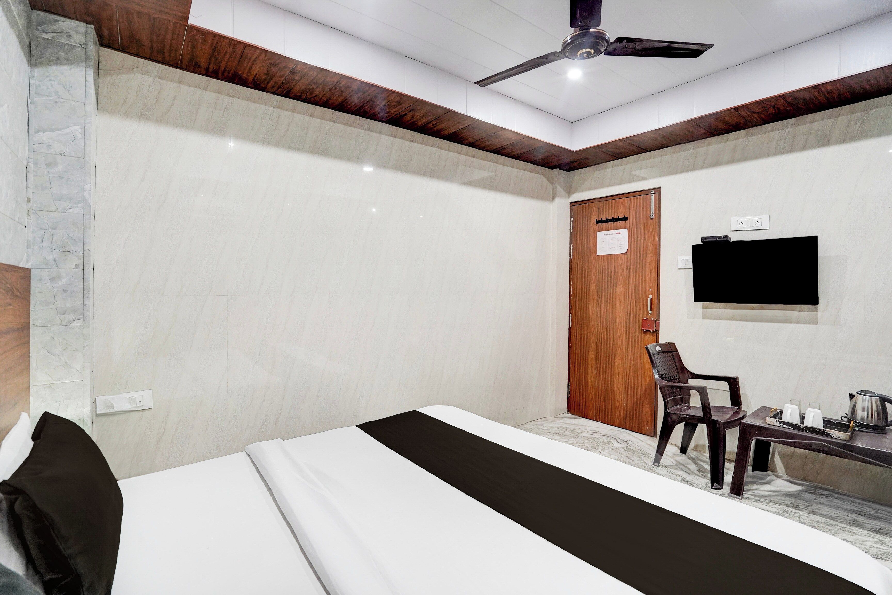 Ein Hotelzimmer mit einem Bett, einem Schreibtisch mit Stuhl, einem Fernseher und einem Deckenventilator.