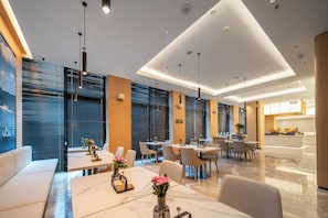 Um saguão de hotel moderno com área de estar, balcão de recepção e vista para a cozinha.