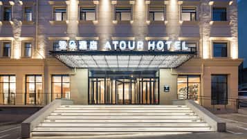 Entrada de hotel con una escalinata monumental, un gran letrero iluminado y una fachada moderna.