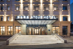 Entrada de hotel con una escalinata monumental, un gran letrero iluminado y una fachada moderna.