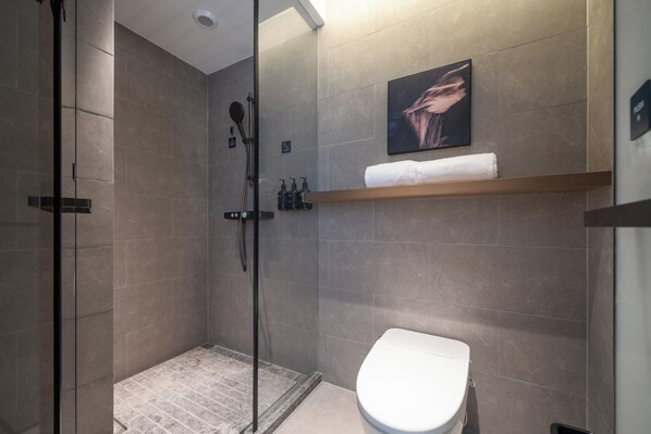 A modern bathroom with a glass shower enclosure, a toilet, and a shelf with toiletries.