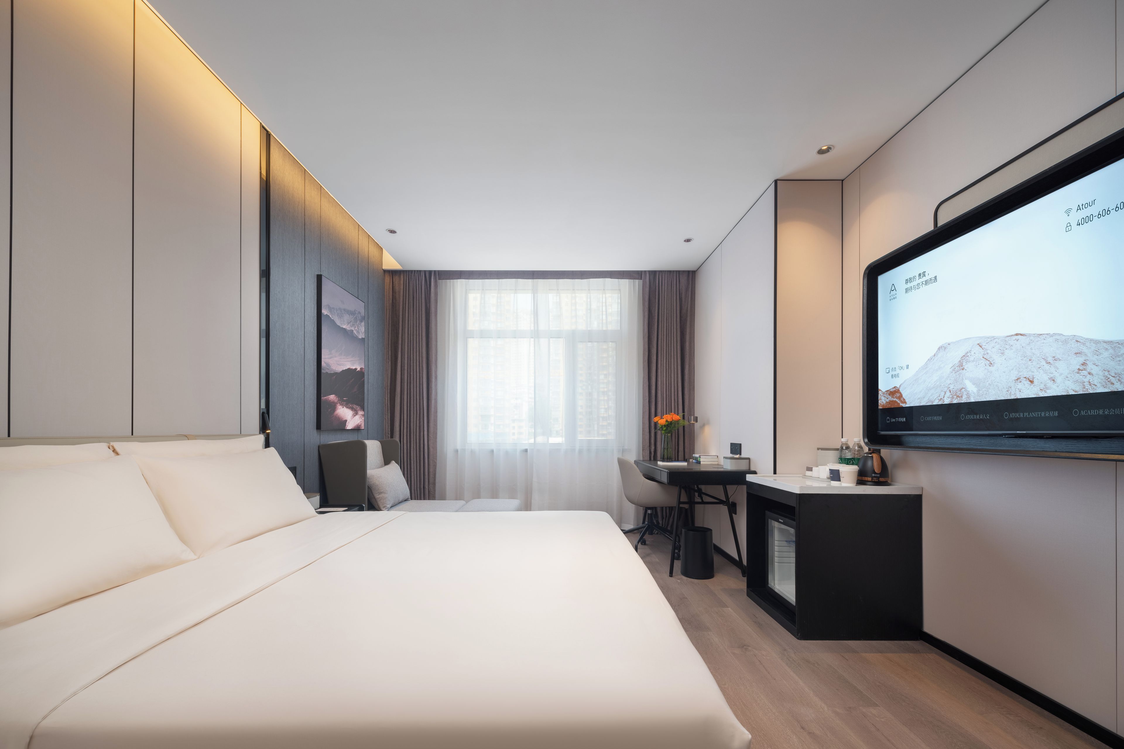 Quarto de hotel moderno com cama, escrivaninha, cadeira, televisão e janela com cortinas.