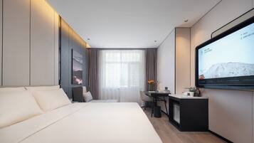 Ein modernes Hotelzimmer mit Bett, Schreibtisch, Stuhl, Fernseher und einem Fenster mit Vorhängen.