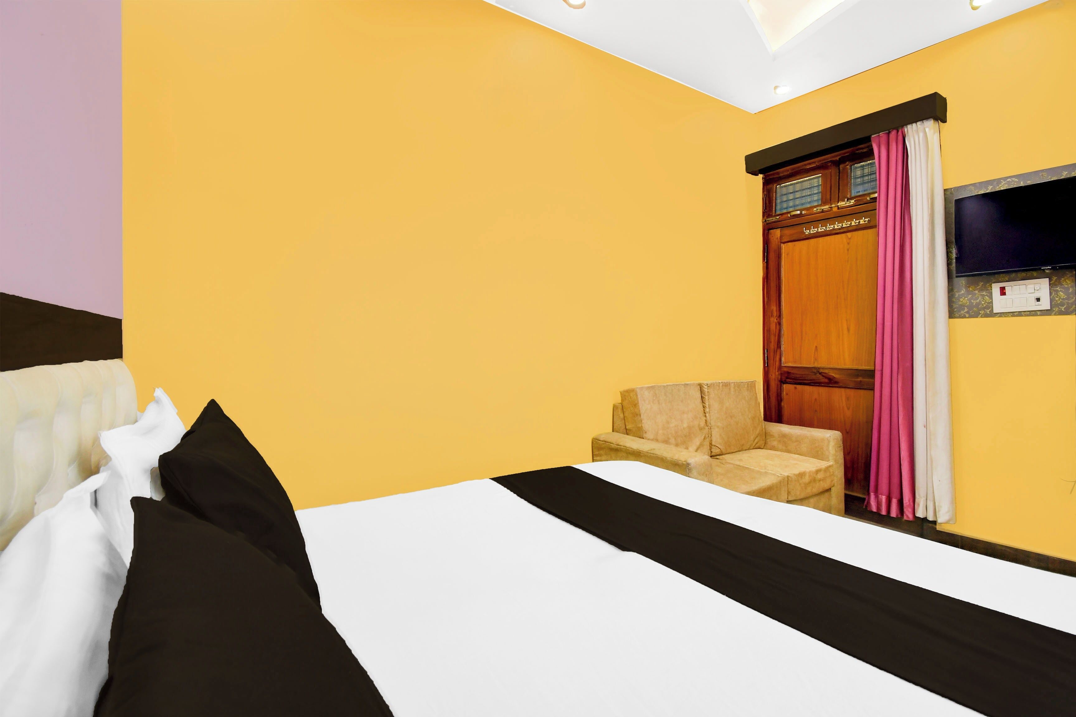 A hotel room with a bed, a chair, a television, and a window with curtains.