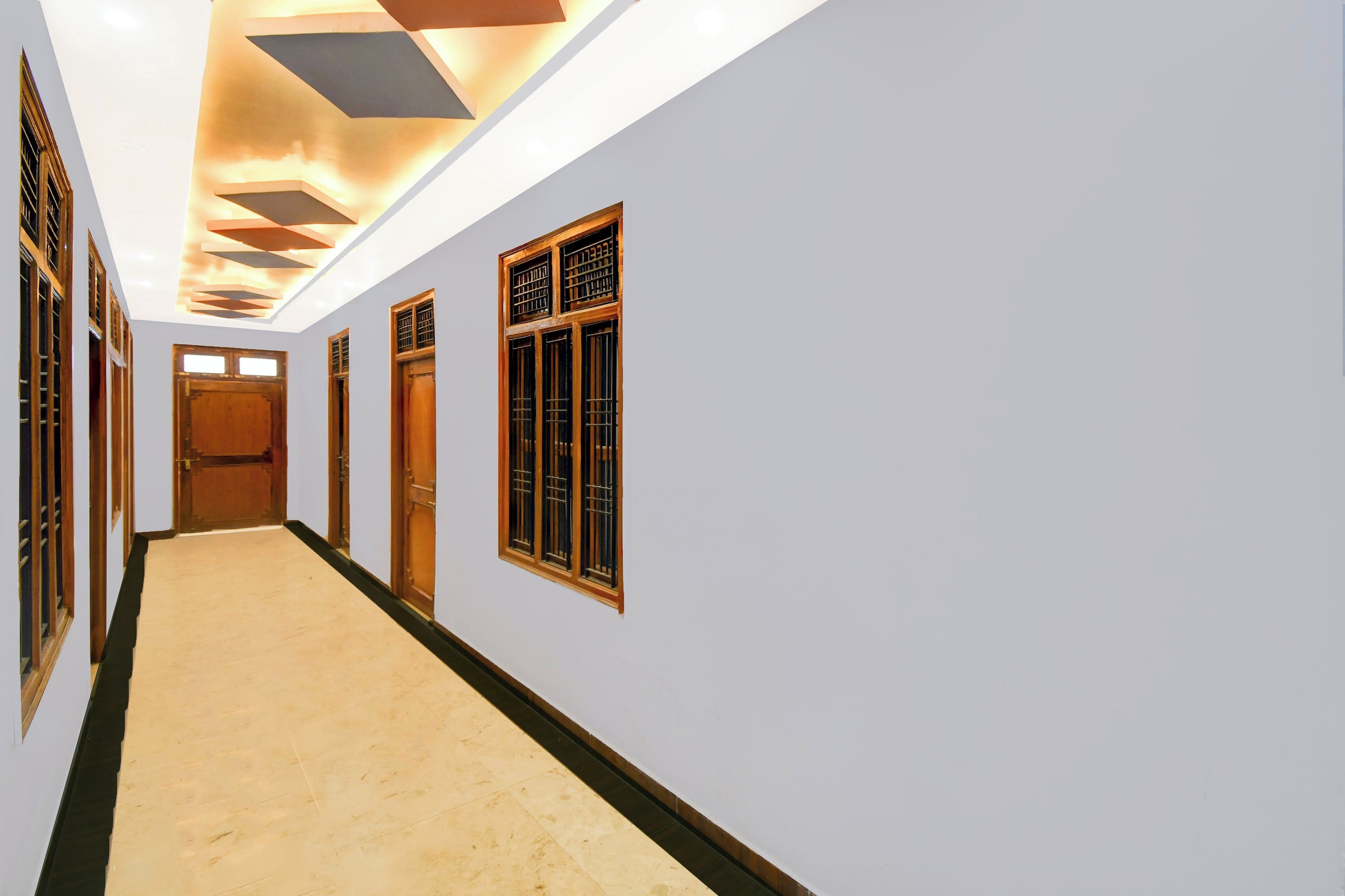 A hallway with a light-colored floor, wooden doors, and windows with metal bars.