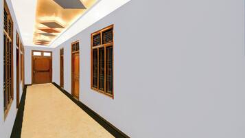 A hallway with a light-colored floor, wooden doors, and windows with metal bars.