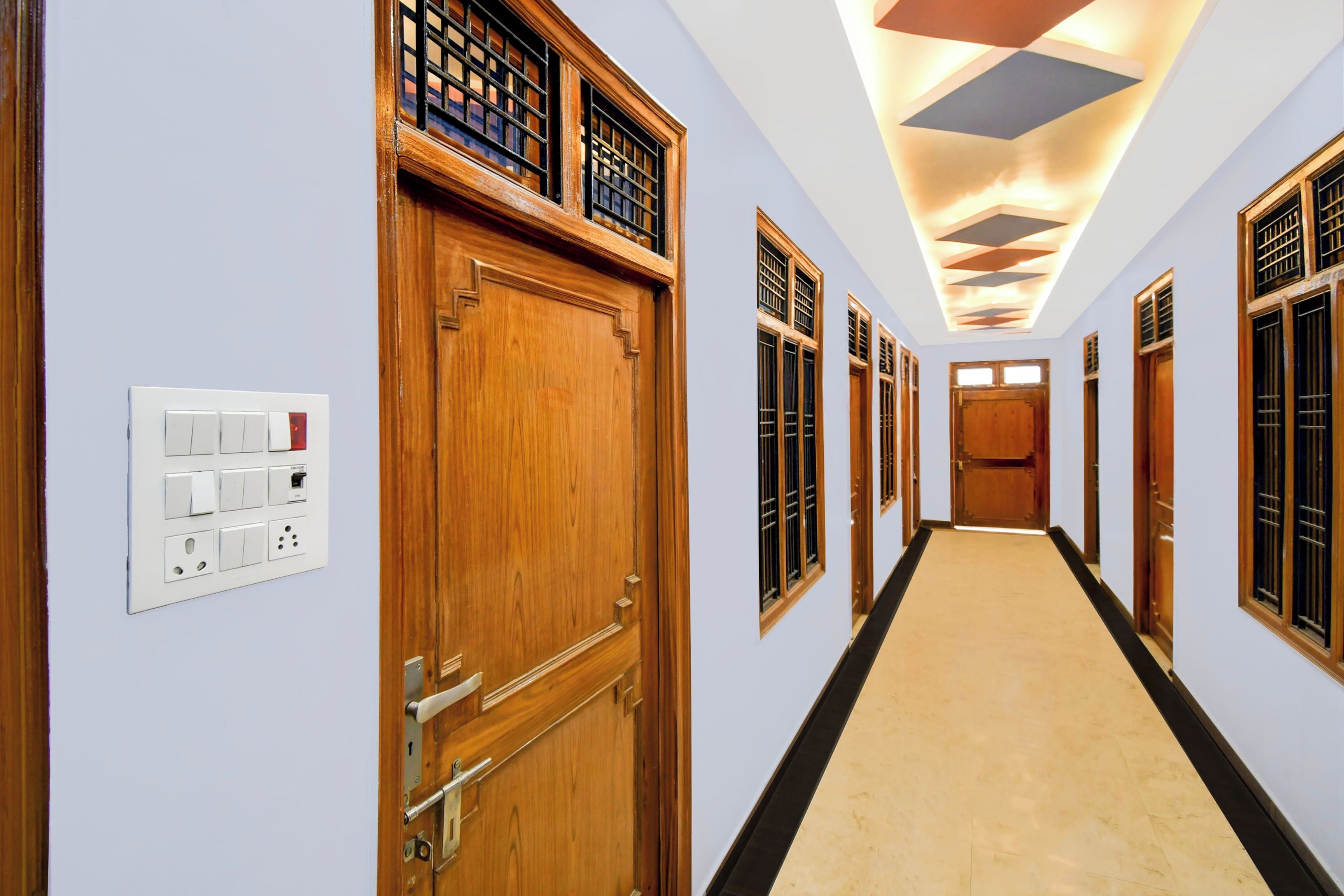 A hotel corridor with wooden doors, a light-colored carpet, and a ceiling with geometric light fixtures.