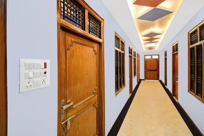 A hotel corridor with wooden doors, a light-colored carpet, and a ceiling with geometric light fixtures.