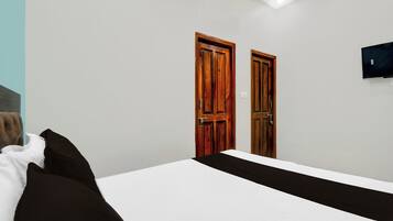 Une chambre à coucher avec un lit, deux portes en bois, un téléviseur fixé au mur et une lucarne.